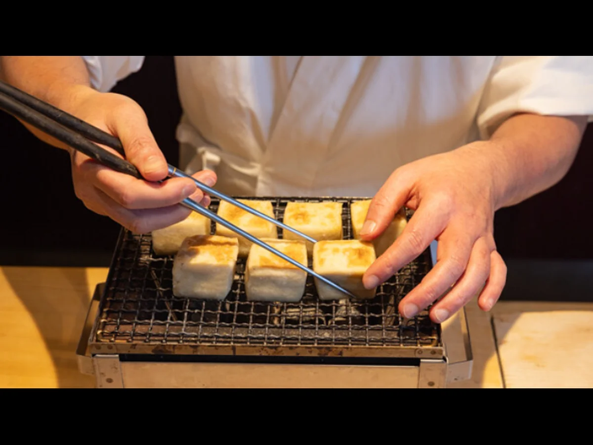 A chef turning rectangular pieces on a tabletop grill at Ginza Uchiyama