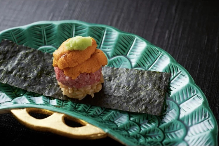 Sea urchin on a pink-centered bite beside sheets of nori on a green plate