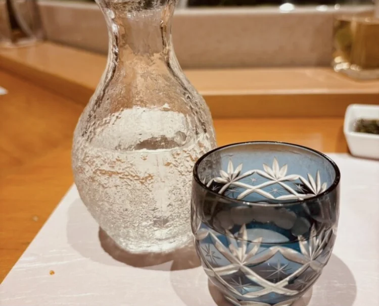 A frosted glass carafe of sake with a blue cut-glass cup