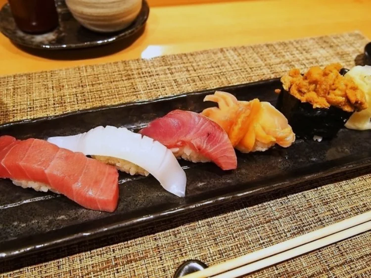A row of five different sushi nigiri on a black ceramic plate